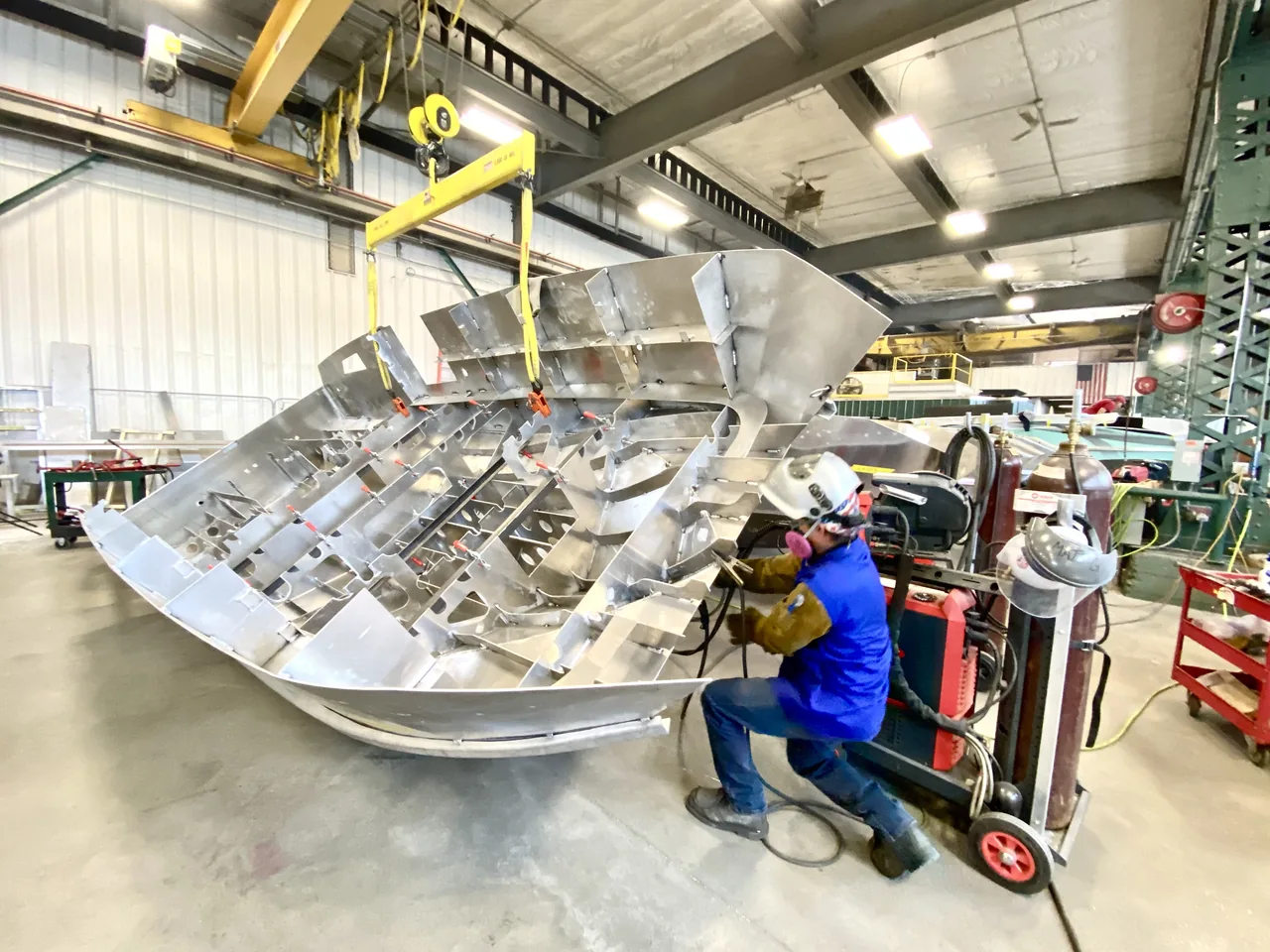 A worker welding an unfinished boat hull in the Armory